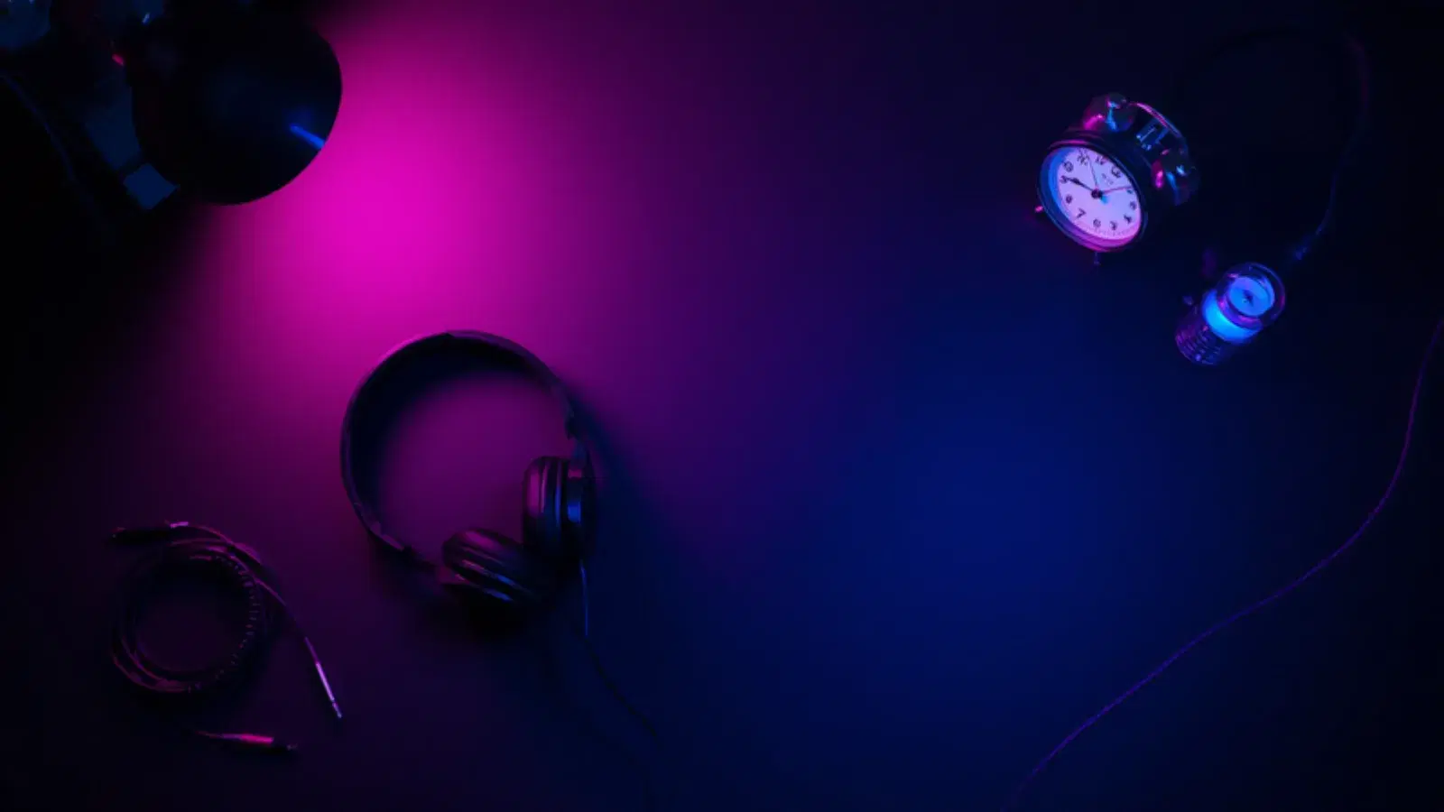 Headphones, a desk clock and a coiled cable on a dark studio table.